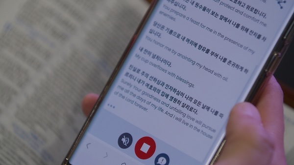 Phone showing live bilingual captions over an open Bible